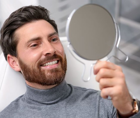 Dental patient holding mirror, admiring his smile