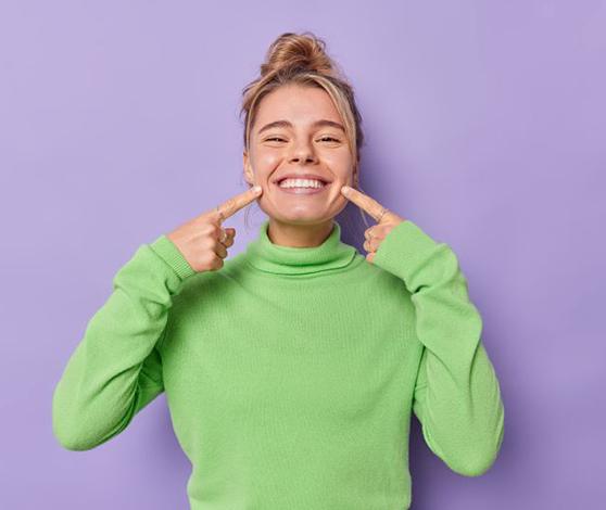 Happy woman in green turtleneck, pointing at her teeth