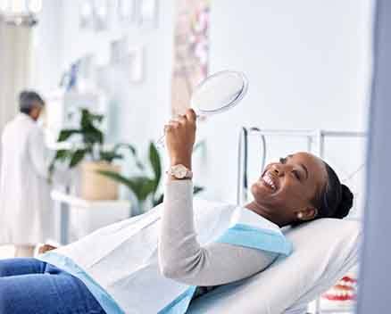 Dental patient reclined in treatment chair, admiring her smile