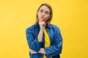 Woman with curious expression on her face, standing against yellow background